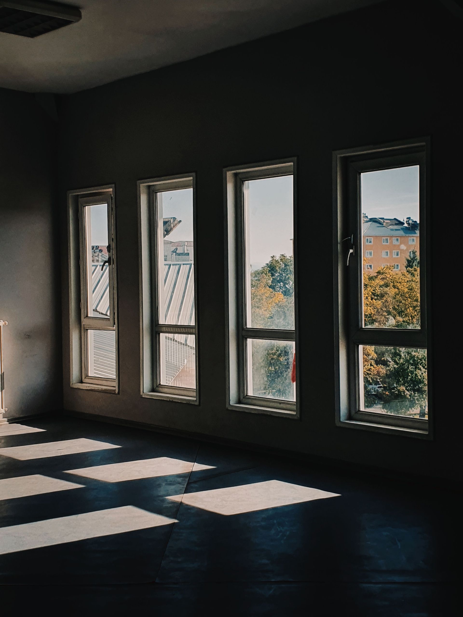 A dark room illuminated by sunlight filtering through five tall windows.